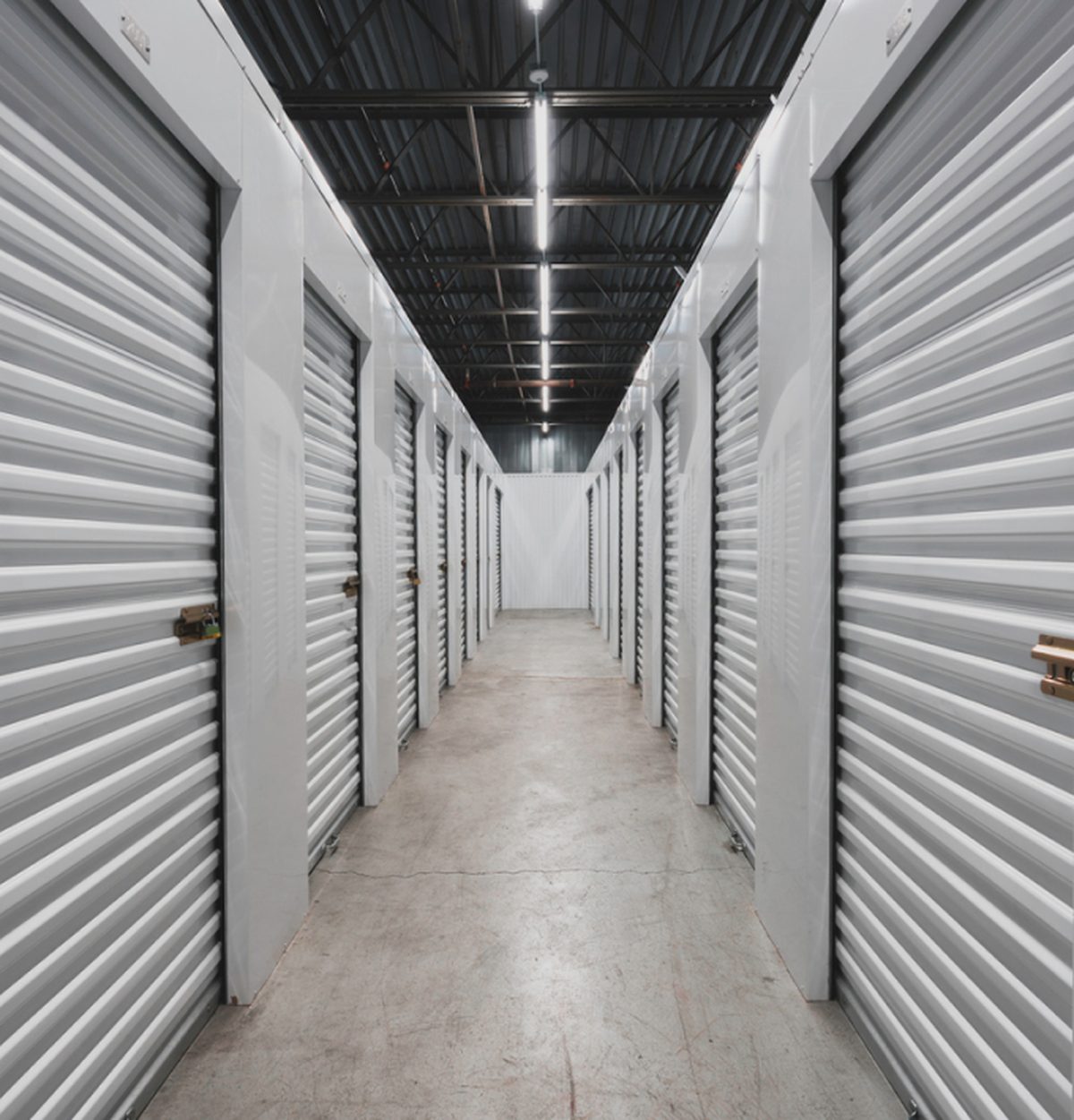 Couloir d'un centre de self-stockage bordé de box aux portes métalliques blanches fermées par cadenas